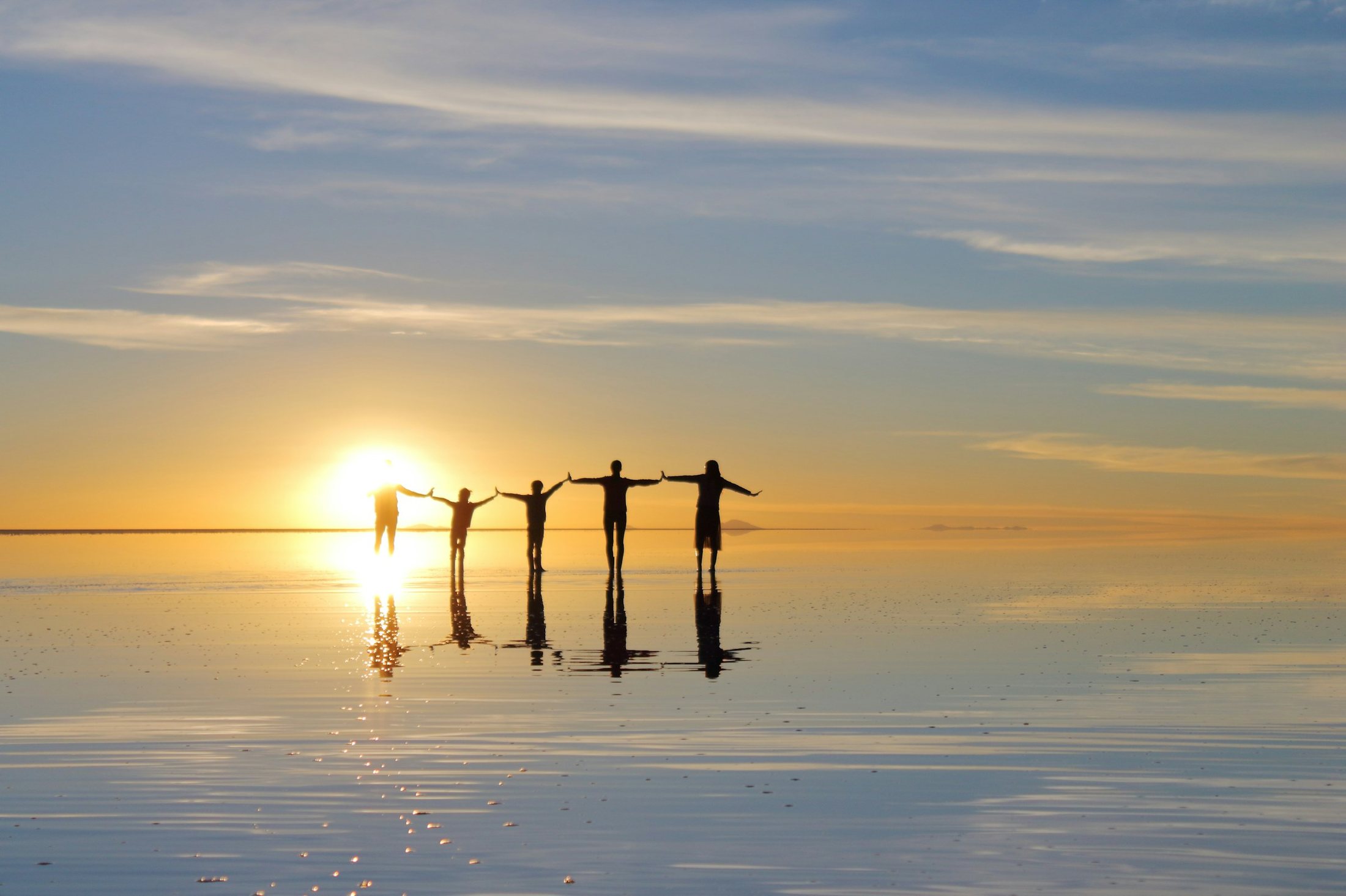Five friends holding hands with arms raised on a beach at sunset